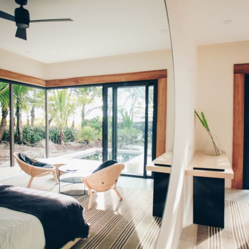 A modern hotel room with large glass sliding doors opening to a tropical garden with palm trees.