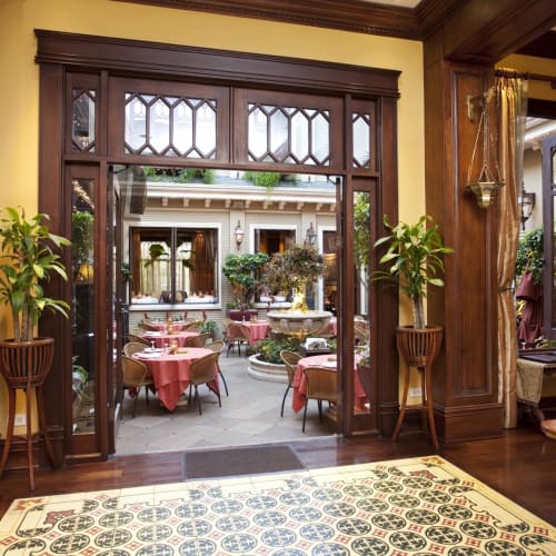 Das Innere eines Restaurants mit Holzvertäfelung und Blick in einen Außenbereich mit runden Tischen und rosa Tischdecken.