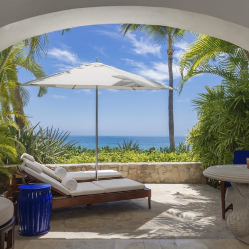 Eine luxuriöse Terrassenfläche am Meer mit Sonnenliege, Sonnenschirm und tropischer Vegetation mit Blick auf das Meer.