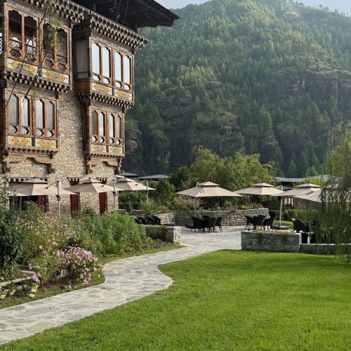 Heritage garden and restaurant with outdoor seating, lush green lawn, and scenic mountains in Bhutan.