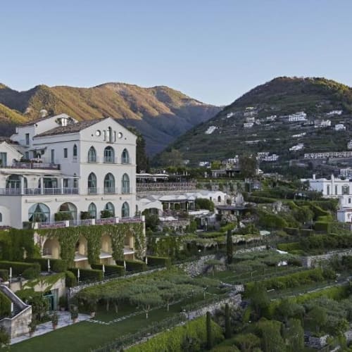 Luxurious white buildings and lush gardens cascade along the Amalfi Coast with green hills in the background.