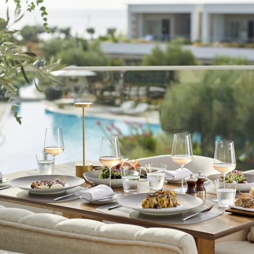 Ein luxuriöser Esstisch im Freien für vier Personen in der Nähe eines Pools, mit Weingläsern, Tellern mit Essen und einer modernen eleganten Dekoration.