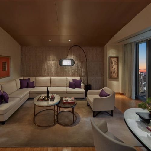 Luxuriöses Wohnzimmer in einer Wohnung in einem Hochhaus mit Stadtblick bei Sonnenuntergang, moderne Möbel und elegante Dekoration.