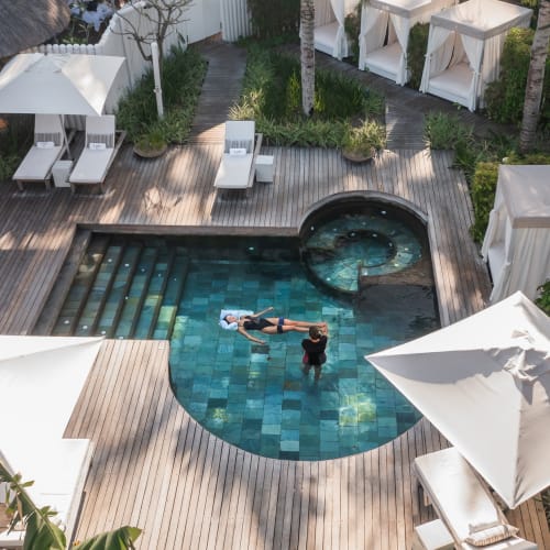 A person relaxing in a swimming pool at a luxurious resort surrounded by lounge chairs and umbrellas.