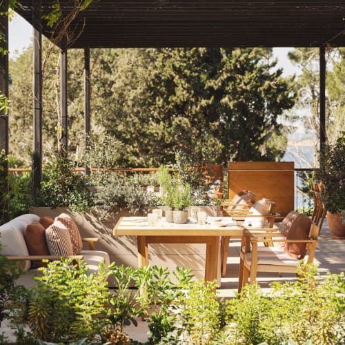 Outdoor dining area at Four Seasons Resort Mallorca with wooden table and chairs under a pergola surrounded by greenery and trees.