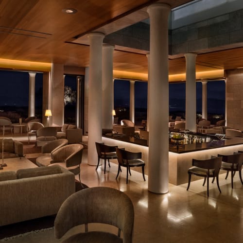 Luxuriöse Bar- und Lounge-Bereich mit modernem Mobiliar, warmem Licht und großen Fenstern mit Blick auf eine dunkle Landschaft.