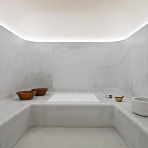 Minimalistischer Spa-Bereich mit weißen Marmorflächen, einer kleinen runden Waschschüssel und einem weißen Handtuch auf einer Ablage, unter sanfter Beleuchtung.