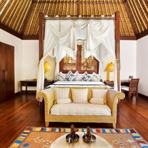 Luxuriöses Schlafzimmer im The Oberoi Beach Resort Lombok mit einem Himmelbett, einem gelben Sofa und Holzmöbeln.