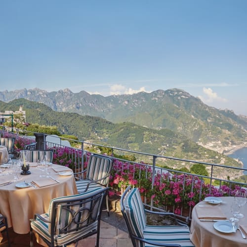 Terrace dining area of Belmond Hotel Caruso with a scenic view of the Amalfi coast and mountains.