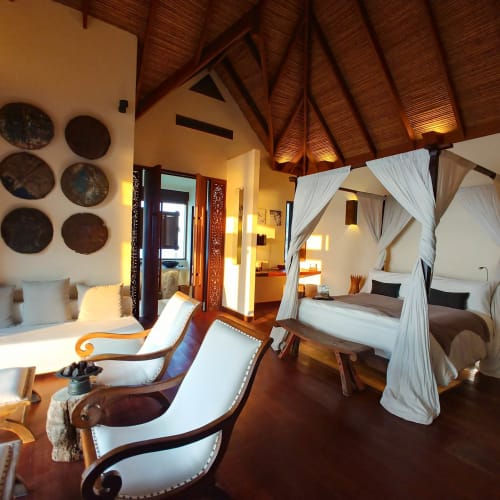 Luxurious bedroom with a four-poster bed and cozy seating area in a tropical villa.