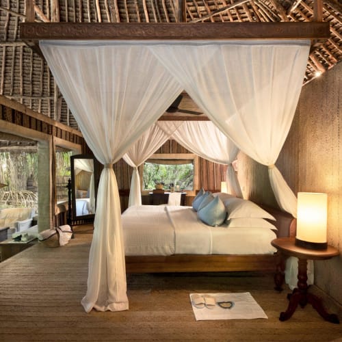 A cozy bedroom with a four-poster bed, soft curtains, and natural wooden furniture in a rustic cottage setting.
