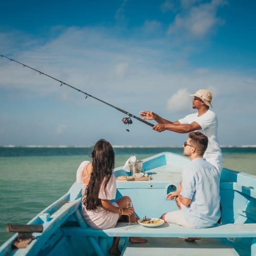 A man and two women are enjoying a fishing trip on a boat in the ocean under a partly cloudy sky.