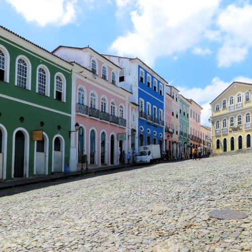 Bunte koloniale Gebäude säumen eine Kopfsteinpflasterstraße mit wenigen Fußgängern unter einem blauen Himmel.