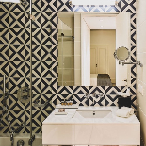 A modern bathroom with geometric black and white tiles, a white sink, and a mirror, with glimpses of the hallway reflected in the mirror.