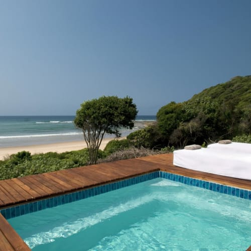 Luxus Außenterrasse mit kleinem Swimmingpool mit Blick auf Strand und Meer, mit üppigem Grün rundherum.