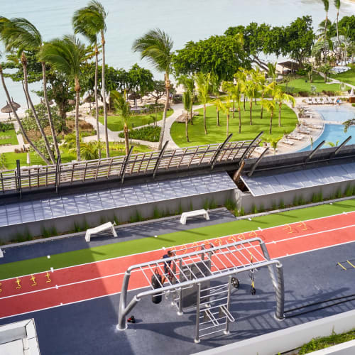 Ein Dachgym mit Blick auf ein tropisches Resort mit Palmen, einem Pool und einem Strand im Hintergrund.