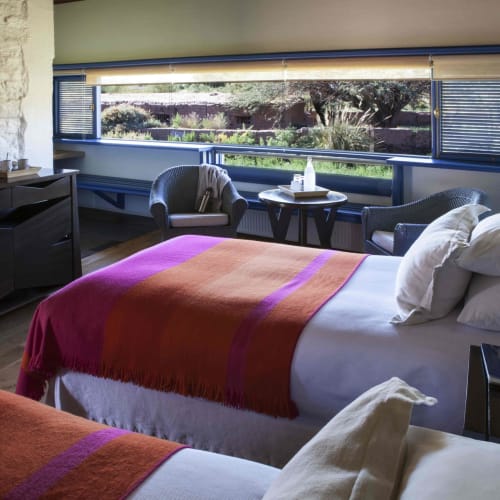 A cozy hotel room with two beds, a large window with a scenic view, and sitting area with chairs and a small table.