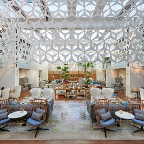 Elegant interior of a restaurant with modern and cozy seating arrangements, decorative ceiling design, and lush greenery in the background.