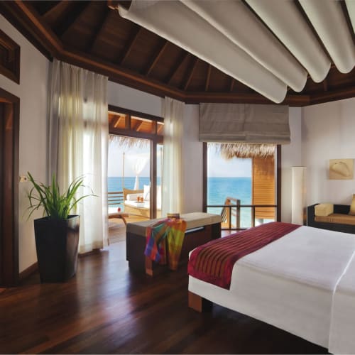 Luxurious bedroom in a water villa with large windows overlooking the ocean, decorated with modern furniture and natural wooden finishes.