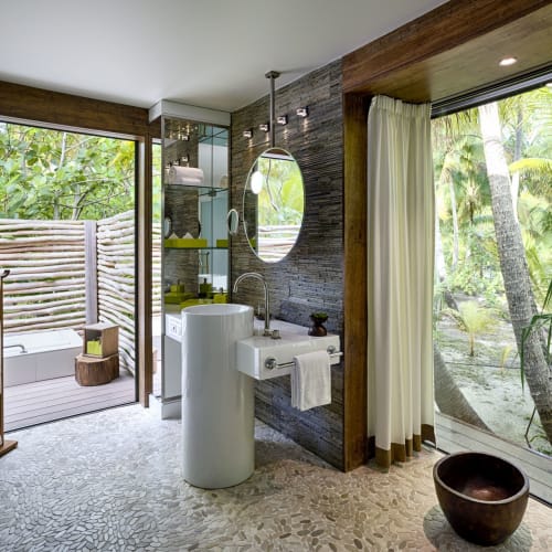 A luxurious hotel bathroom with large sliding glass doors opening to a lush tropical garden.