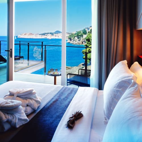 Ein Schlafzimmer mit großem Bett, das durch Glas-Schiebtüren auf das Meer blickt, mit Balkon draußen und malerischem Wasserblick.