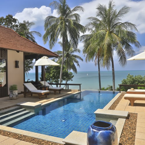 Private Poolvilla mit zwei Schlafzimmern am Meer mit Blick auf den Pool, Liegestühlen und Palmen unter blauem Himmel.