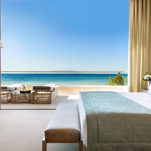 Luxuriöses Schlafzimmer in einer Suite mit großem Balkon mit Blick auf das Meer, dekoriert mit neutralen Tönen und eleganten Möbeln.