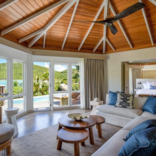 Ein luxuriöser Wohnzimmer mit großen Glasschiebtüren, die auf eine grüne Landschaft und den Poolblick öffnen, mit Holzdecke und bequemen Sitzmöbeln.