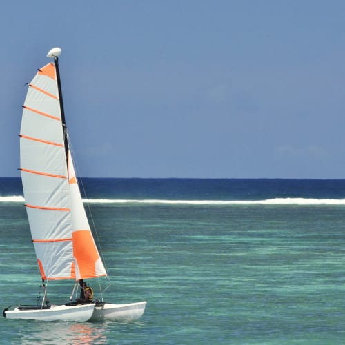 A sailboat with a colorful sail glides on clear turquoise water near the coast.