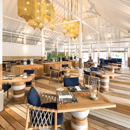 Elegant restaurant with wooden tables and chairs, contemporary lighting, and a bright, airy interior with large windows overlooking lush greenery.