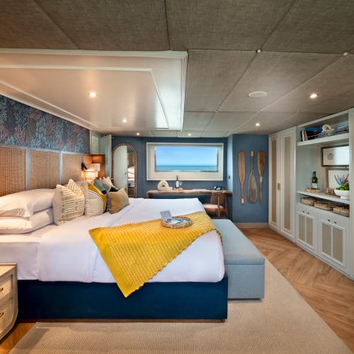 Luxurious bedroom with a large bed, colorful pillows, and ocean view through a window in a well-decorated suite.