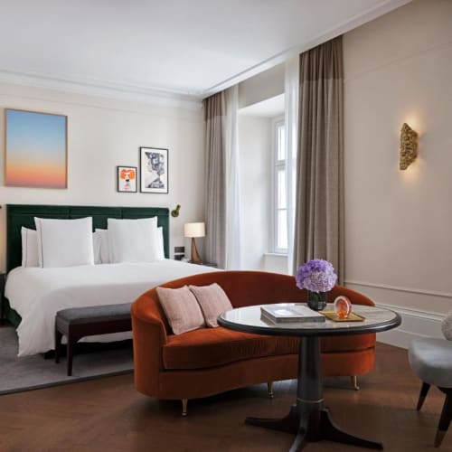 A luxurious hotel room with a large bed, sitting area with a round table, and elegant decor.