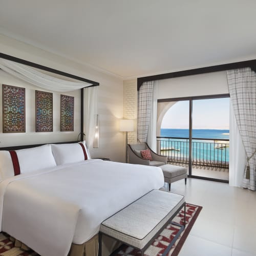 Luxurious hotel room with a large bed, balcony with sea view, and elegant decor in Jordan.