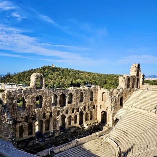 Ancient Herodes Atticus Odeon amphitheatre in Athens with stone seating and arched stone walls under a clear blue sky.