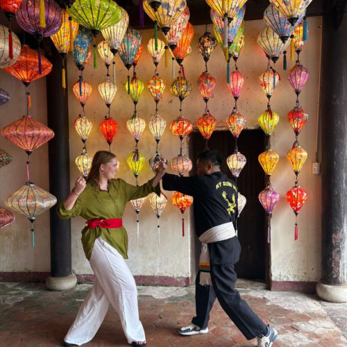 Zwei Personen üben Kampfsport unter einer Decke mit bunten hängenden Laternen in einer traditionellen vietnamesischen Umgebung.
