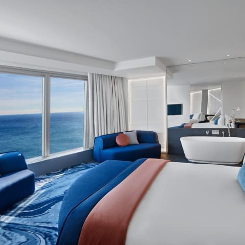 Luxurious bedroom with a large bed, blue sofas, and an expansive ocean view through the windows in a modern suite.