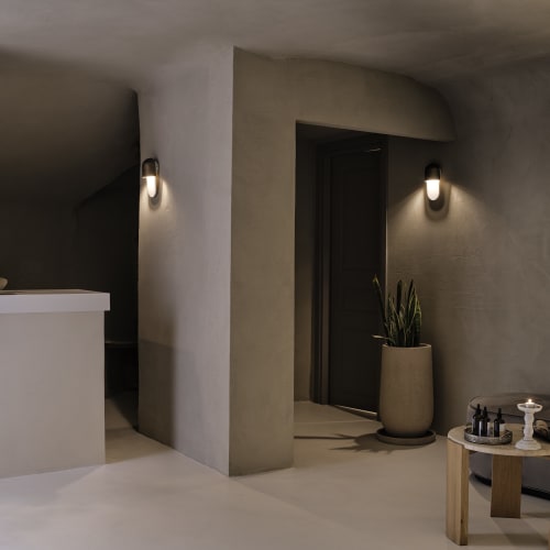 Minimalist spa reception area with soft ambient lighting, featuring a small table with spa products, a potted plant, and smooth beige walls.