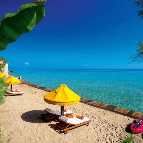 Sonnenliegen mit gelben Sonnenschirmen an einem Sandstrand mit Blick auf klares blauer Wasser.