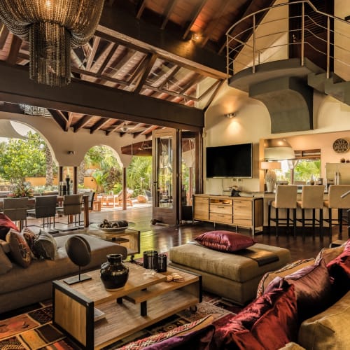 Luxuriöses Wohnzimmer mit bequemen Sofas, einer modernen Treppe und einem offenen Bereich, der zu einer Terrasse im Freien mit Grünfläche führt