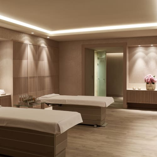 Ein Spa-Massageraum mit zwei Massageliegen, sanftem Licht und dekorativen Blumen auf Tischen.