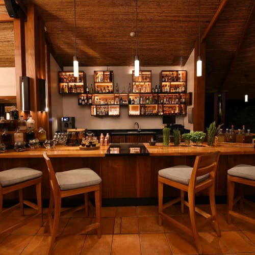 A cozy bar area inside a warm-toned resort with wooden furniture and shelves filled with bottles in the background.