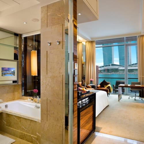 Ein luxuriöses Hotelzimmer mit Meerblick, ausgestattet mit einem Sofa, einem Schreibtisch und großen Fenstern mit Blick auf das Wasser.