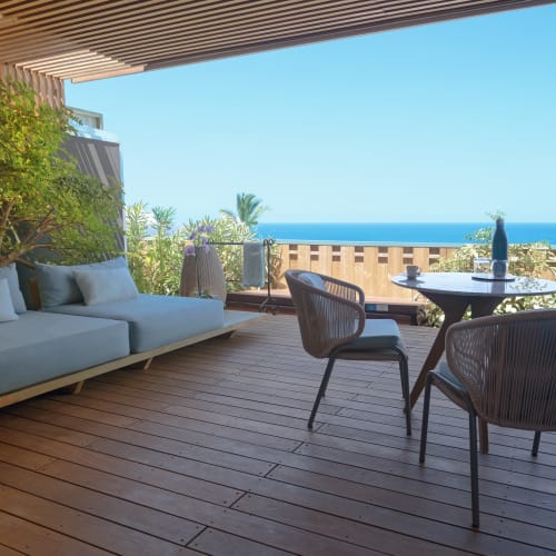 Gemütliche Außenterrasse mit modernem blauen Polstersofa, rundem Tisch und zwei Stühlen mit Blick auf das klare blaue Meer unter sonnigem Himmel.