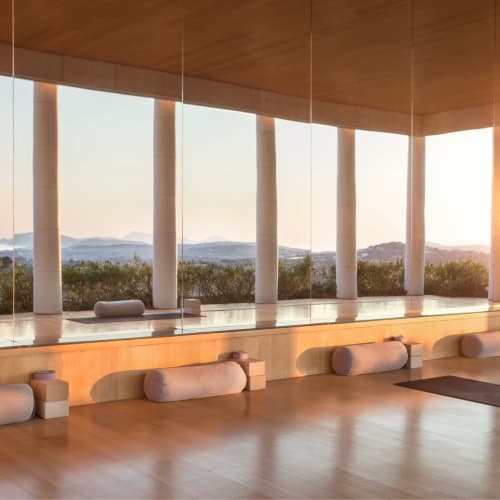Ein geräumiger Yoga-Pavillon mit Holzdecke und großen Fenstern mit Blick auf eine landschaftliche Szenerie bei Sonnenuntergang.