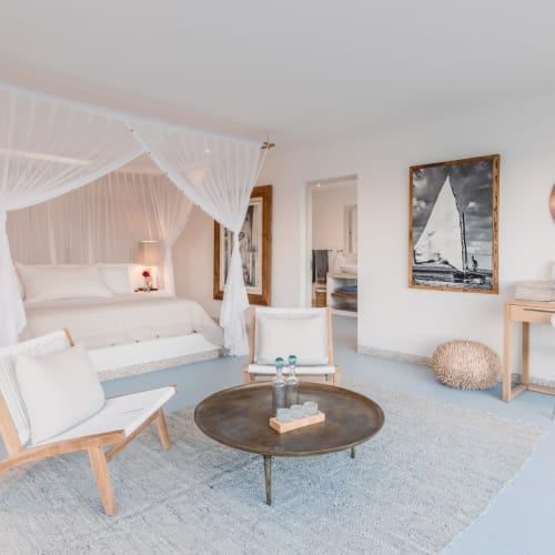 Ein heller, eleganter Hotellzimmer mit Himmelbett, minimalistischer Einrichtung und nautisch inspiriertem Kunstwerk im Hintergrund.