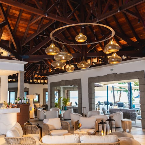 Geräumiger Resort-Lounge-Bereich mit Korbmöbeln, mehreren runden gepolsterten Sesseln, einem modernen Kronleuchter mit rundem Holzrahmen und einer hölzernen gewölbten Decke mit großen Fenstern zum Außenpool.