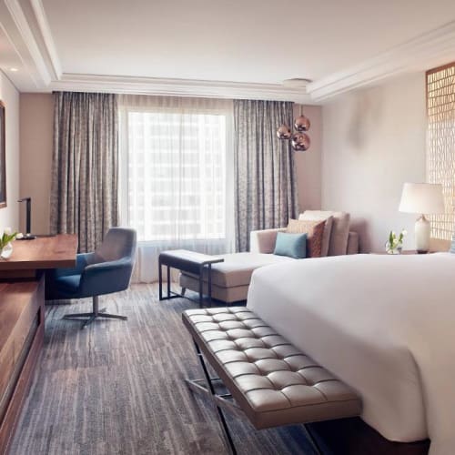 Gemütliches Hotelzimmer mit einem großen Bett, Sitzbereich und Schreibtisch vor einem Fensterausblick, modern eingerichtet.