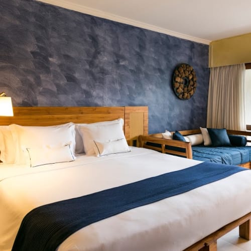 Ein gemütliches Hauptschlafzimmer mit großem Bett, Holzkopfteil und einer kleinen Sitzecke in der Nähe eines großen Fensters mit Blick auf die Natur.