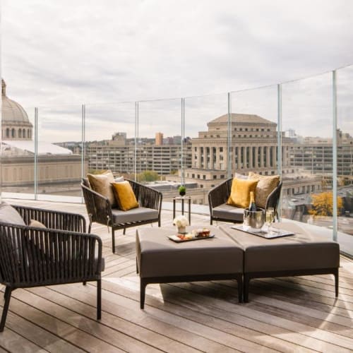 Elegante Dachterrasse mit schwarzen Korbsesseln, einem grauen Ottoman und gelben Kissen mit Blick auf die Bostoner Skyline.
