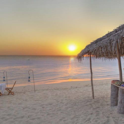 Sonnenuntergang am Strand auf der Azura Quilalea Private Island mit Strandstühlen und einer strohgedeckten Strandbar.